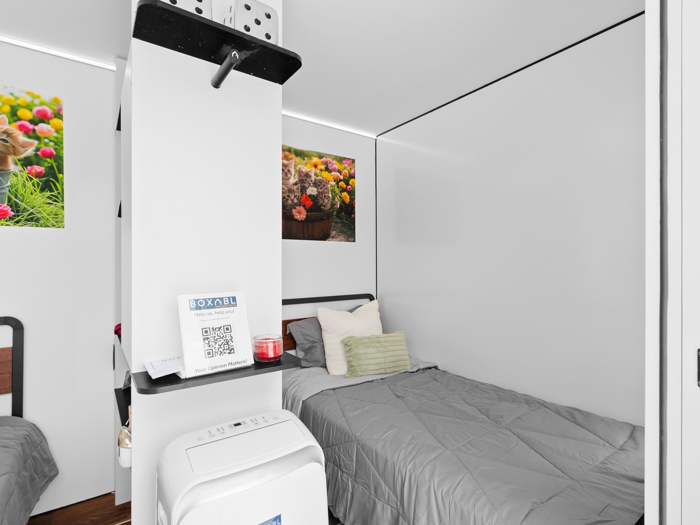 Interior of a Sanctuary unit showing a made bed, shelf, and portable climate unit